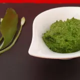 Un bol de pesto vert vif à l'ail des ours, accompagné de quelques feuilles et boutons de la plante.