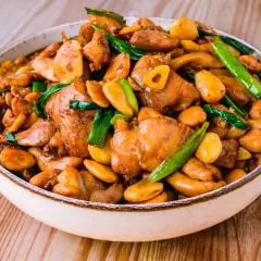 Un plat appétissant de poulet noix de cajou, garni d'oignons verts et d'ail, dans un bol sur une table en bois.
