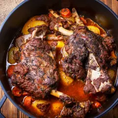 Deux épaules d'agneau en cocotte, tendres et savoureuses, mijotent avec des pommes de terre et des carottes dans un jus parfumé.