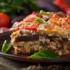 Un généreux flan de légumes, aux couches d'aubergines et de tomates, garni de basilic frais, sur une assiette en terre cuite.