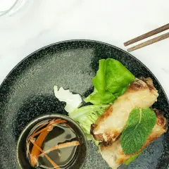 Deux nems dorés sur un lit de salade, accompagnés d'une coupelle de sauce nem maison et de baguettes.