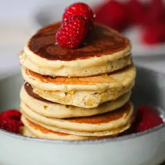 Pile de délicieux pancake sans gluten, garnis de framboises fraîches et nappés de sirop.