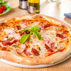 Une délicieuse pâte à pizza garnie de jambon, de tomates séchées et de basilic frais, prête à être dégustée.