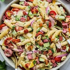 Salade de pâtes généreuse avec penne, tomates cerises, concombre, salami et oignons rouges. Un plat frais et coloré.