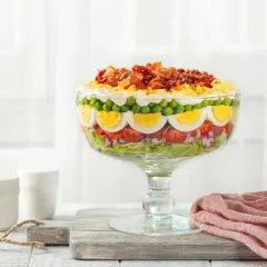 Une magnifique salade 7 étages, présentée dans un grand bol en verre, avec des couches de légumes frais, d'œufs durs, de petits pois et de bacon croustillant sur le dessus.