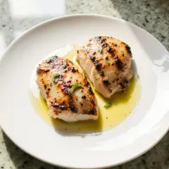 Deux morceaux de blanc de poulet airfryer, dorés et juteux, servis sur une assiette blanche avec un filet d'huile et quelques herbes.