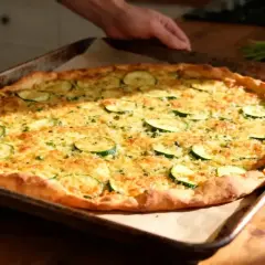 Une galette de courgette dorée et appétissante, garnie de fines rondelles de courgettes et de fromage râpé, sort du four.