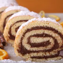 Tranches de roulé au chocolat saupoudrées de sucre glace, accompagnées d'oranges et de bâtons de cannelle.