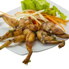 Assiette de cuisses de grenouille grillées, garnie de salade verte, d'oignons et de carottes râpées.