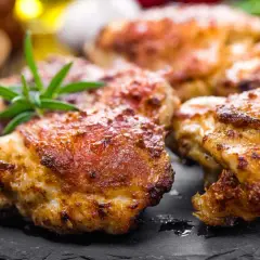Délicieuses cuisses de poulet Cookeo dorées et croustillantes, garnies de romarin frais sur une assiette en ardoise.