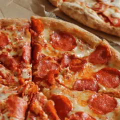 Deux pizzas au pepperoni, l'une coupée en parts, sur une pâte à pizza fine et croustillante.