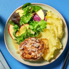 Un steak haché sauce oignons, servi avec une généreuse portion de purée de pomme de terre et une salade croquante aux pommes.