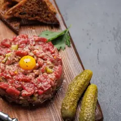 Un délicieux tartare de boeuf, garni d'un jaune d'œuf, servi avec des cornichons, du pain grillé et des épices.