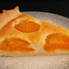 Tranche de tarte aux abricots classique, avec sa pâte dorée et ses fruits juteux, prête à être dégustée.