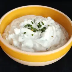 Sauce onctueuse à base de fromage blanc et de ciboulette fraîche, garnie de brins d'herbe verte.