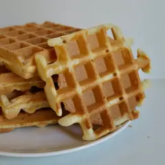 Pile de gaufres dorées sur une assiette blanche. La pâte à gaufre a été cuite à la perfection, offrant une texture croustillante et moelleuse.