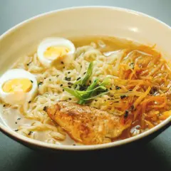 Un bol de recette ramen poulet, garni d'œufs durs, de poulet grillé, de nouilles et de ciboule.