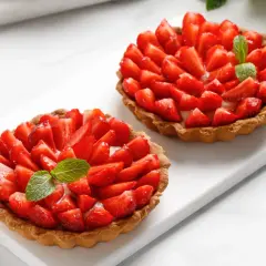 Deux tartelettes gourmandes aux fraises fraîches et crème pâtissière, ornées d'une feuille de menthe. Un délice estival.