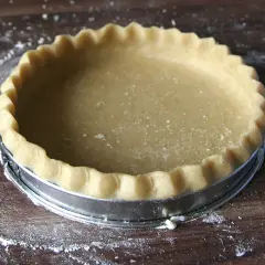 Une pâte brisée maison, prête à être garnie, repose dans un moule à tarte sur une planche en bois.