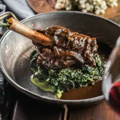 Un gigot de 7 heures, tendre et savoureux, servi sur un lit d'épinards crémeux dans un plat en cuivre. Une touche de romarin sur l'os promet un délice.