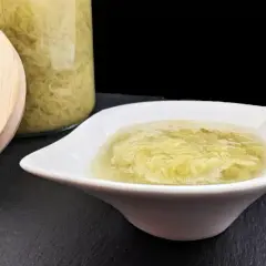 Compote de rhubarbe maison dans un bol blanc, à côté d'un bocal en verre rempli de cette délicieuse préparation.