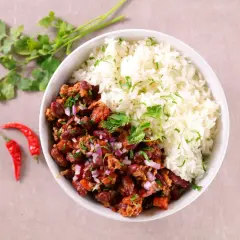 Un bol de chili con carne et riz, garni de persil frais et d'oignons rouges. Deux piments rouges sont posés à côté.