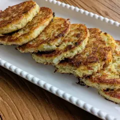 Six galettes de pomme de terre dorées et croustillantes, disposées sur un plat blanc festonné, prêtes à être dégustées.