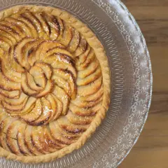 Tarte aux pommes magnifiquement arrangée en spirale sur un plat en verre, prête à être dégustée.