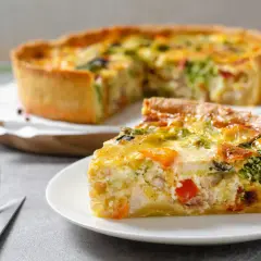 Une part de quiche savoureuse, garnie de poulet, brocolis et poivrons, repose sur une assiette. La pâte à quiche dorée est parfaite.