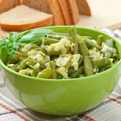 Salade haricots verts fraîchement préparée, garnie de basilic, servie dans un bol vert vif.