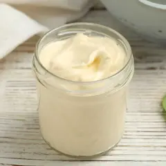 Un pot en verre rempli d'une onctueuse mayonnaise sans huile, sur une table en bois. Une feuille verte à côté.
