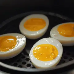 Quatre moitiés d'oeuf dur, avec un jaune coulant, sont disposées dans un airfryer.
