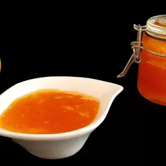 Un abricot frais à côté d'une coupelle de confiture abricot peu sucrée et d'un bocal de cette même confiture.