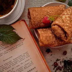 Crêpes roulées sur une assiette, accompagnées d'une tasse de thé et d'un livre de recette. Une framboise décore les crêpes. Parfait pour une recette crêpe.