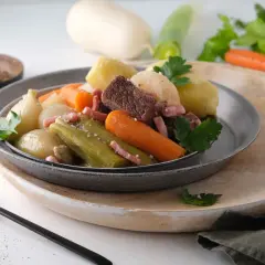 Pot-au-feu Cookeo avec viande, légumes (carottes, poireaux, oignons) et lardons, servi dans une assiette grise.