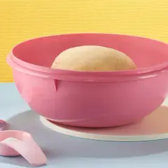Pâte à pain dans un bol Tupperware rose, prêt pour une recette minute. À côté, un téléphone vintage, des cuillères doseuses et une bouteille d'eau.