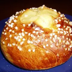 Mouna dorée parsemée de sucre perlé sur une assiette bleue.