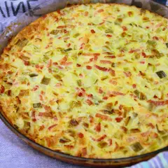 Une quiche aux légumes dorée et appétissante, garnie de poireaux et de lardons, sortant du four dans un plat en verre.
