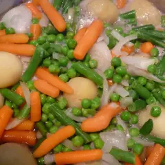 Gros plan sur une jardinière de légumes bouillant : carottes, petits pois, haricots verts, pommes de terre et oignons.