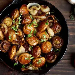 Champignons de Paris sautés à l'ail et aux oignons dans une poêle en fonte, parfaits pour une recette simple et savoureuse.