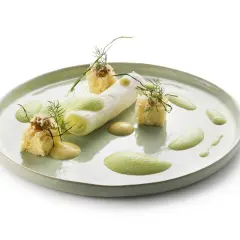 Poireaux à la crème, présentés avec des cubes de pain brioché, une sauce crémeuse et une mousse verte aérienne, le tout garni d'aneth.