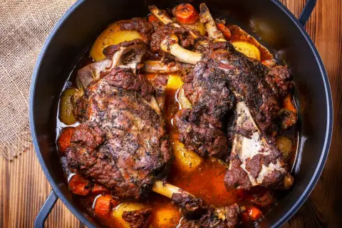 Deux épaules d'agneau en cocotte, tendres et savoureuses, mijotent avec des pommes de terre et des carottes dans un jus parfumé.