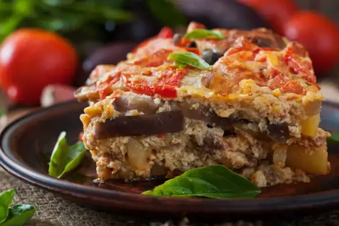 Un généreux flan de légumes, aux couches d'aubergines et de tomates, garni de basilic frais, sur une assiette en terre cuite.