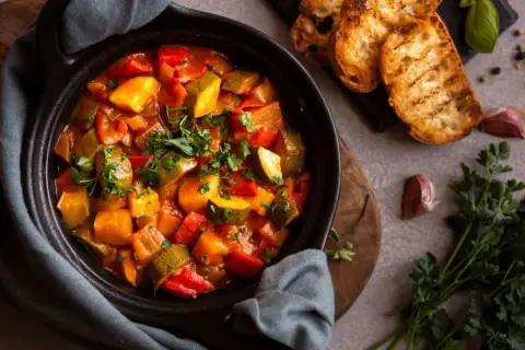 Ratatouille colorée dans un plat noir, servie avec des toasts grillés. Parfait pour savoir que manger avec une ratatouille.