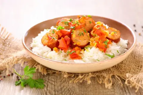 Un plat de rougail saucisse savoureux, avec des morceaux de saucisses épicées sur un lit de riz blanc, garni de persil frais.