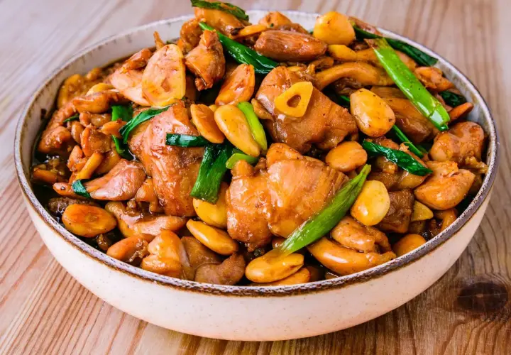 Un plat appétissant de poulet noix de cajou, garni d'oignons verts et d'ail, dans un bol sur une table en bois.