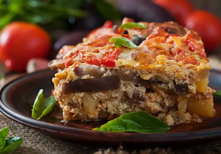 Un généreux flan de légumes, aux couches d'aubergines et de tomates, garni de basilic frais, sur une assiette en terre cuite.
