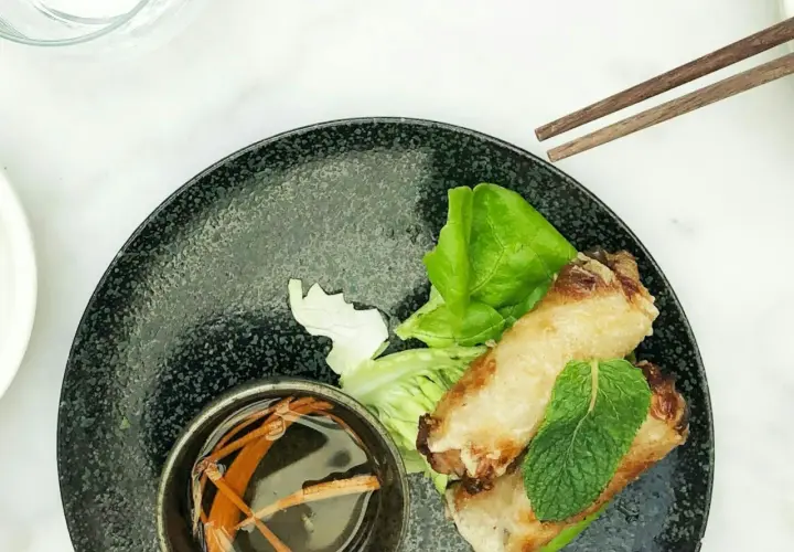 Deux nems dorés sur un lit de salade, accompagnés d'une coupelle de sauce nem maison et de baguettes.