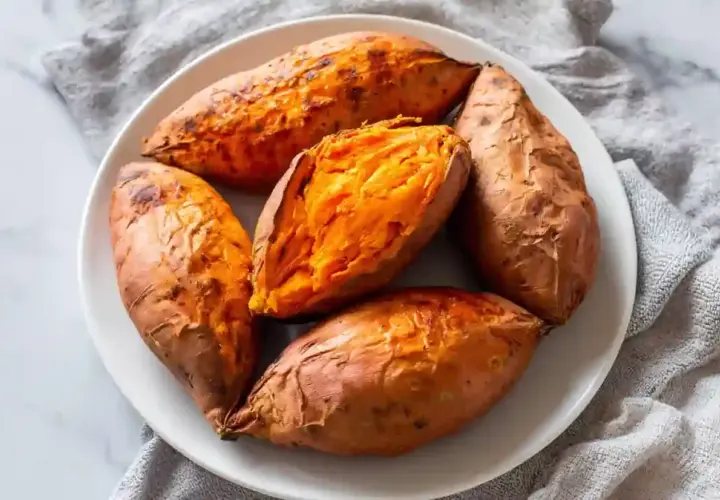 Cinq patates douces rôties à la perfection dans un air fryer, servies sur une assiette blanche. L'une est coupée en deux, révélant sa chair orange tendre.