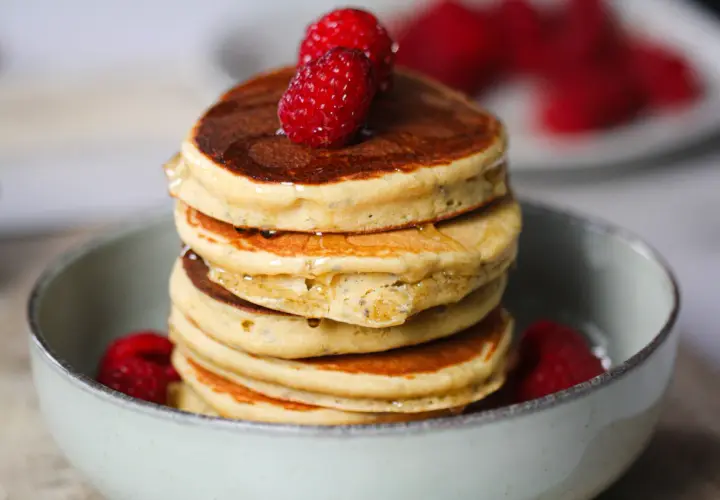 Pile de délicieux pancake sans gluten, garnis de framboises fraîches et nappés de sirop.
